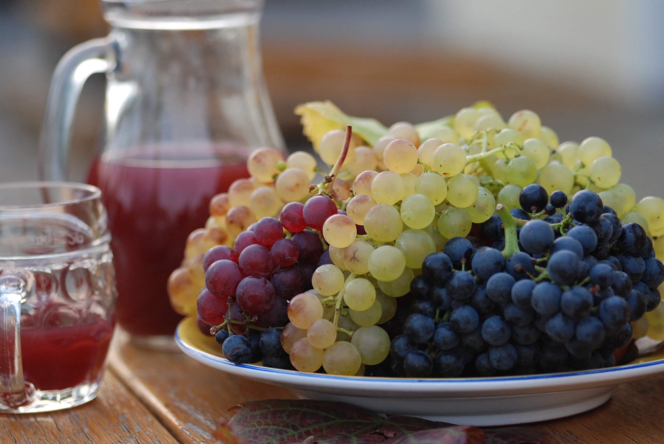 Verschiedenfarbige Weintrauben auf einem Teller mit Most im Hintergrund