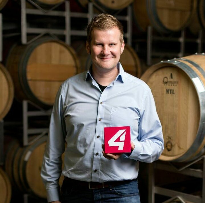 Andreas Grosz vor Weinfässern und Puls4 Logo in der Hand